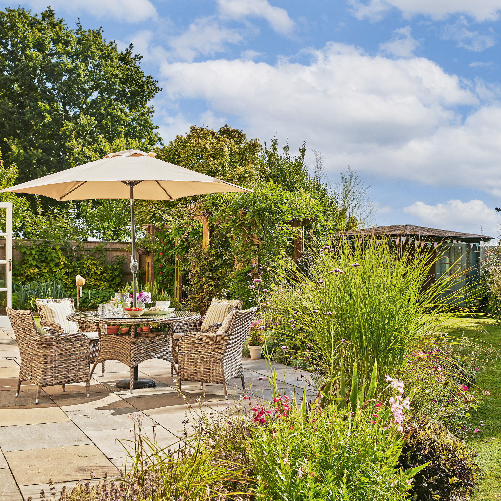 a patio with dining furniture and parasol alongside a lawn and summerhouse