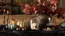 Table with black tablecloth, skull and pumpkin ornaments, a glass cloche and black taper candles