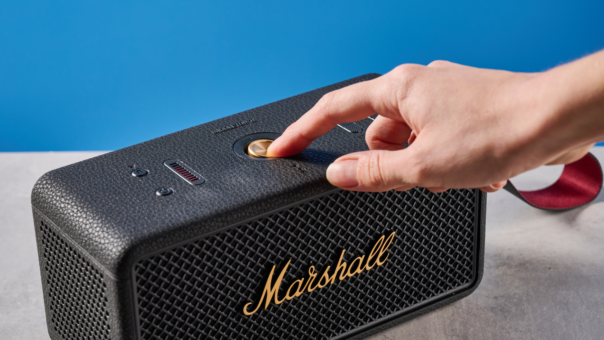 The Marshall Middleton II Bluetooth speaker in Black and Brass, on a stone surface with a blue wall in the background