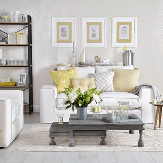 grey and yellow living room with white couches, grey nested coffee tables, photo frames on the wall and a black and brown display unit
