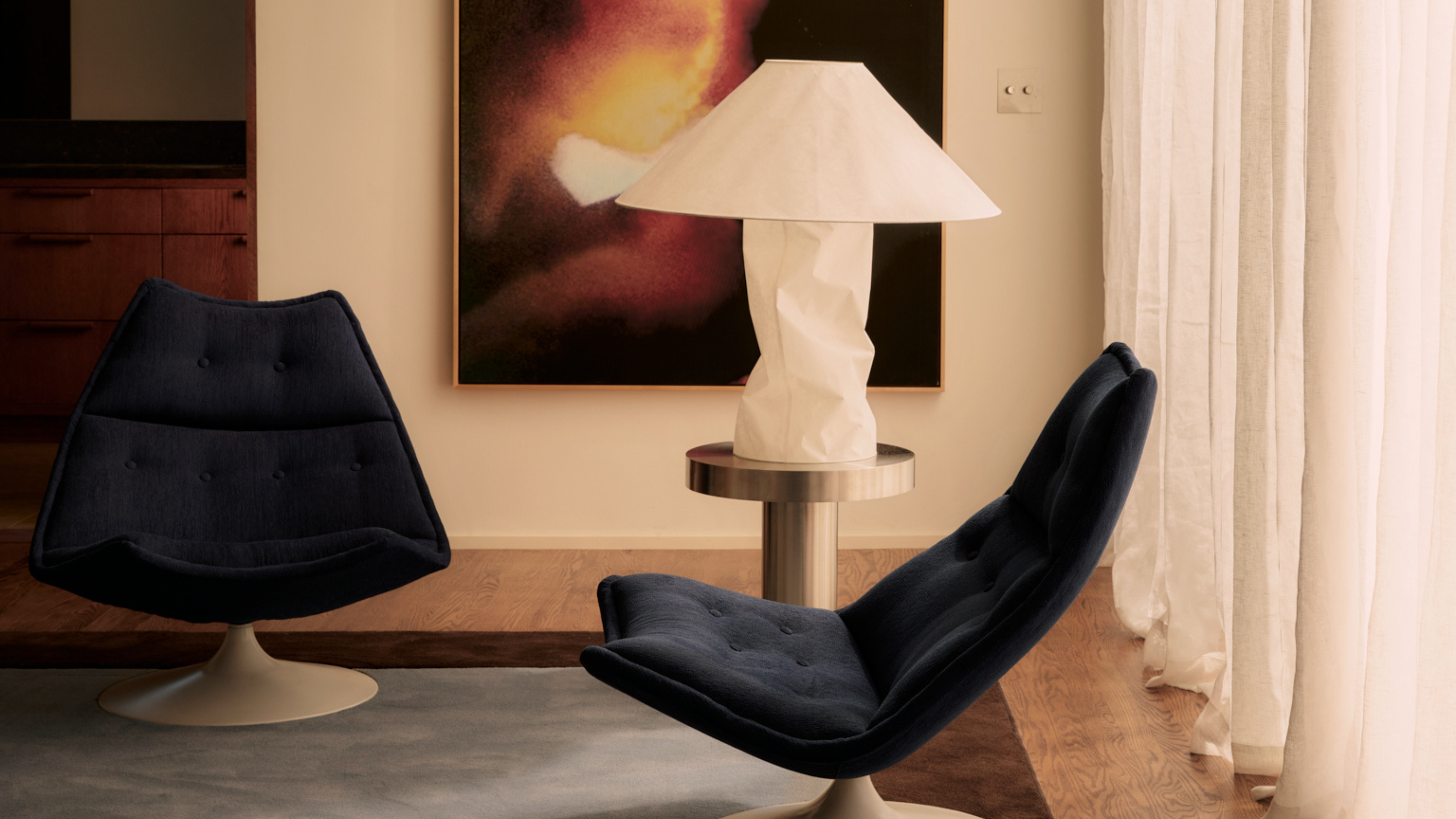 A crumpled paper table lamp next to two navy arm chairs in a living room