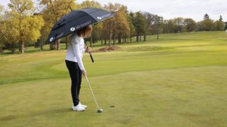 Alison Root putting while holding umbrella