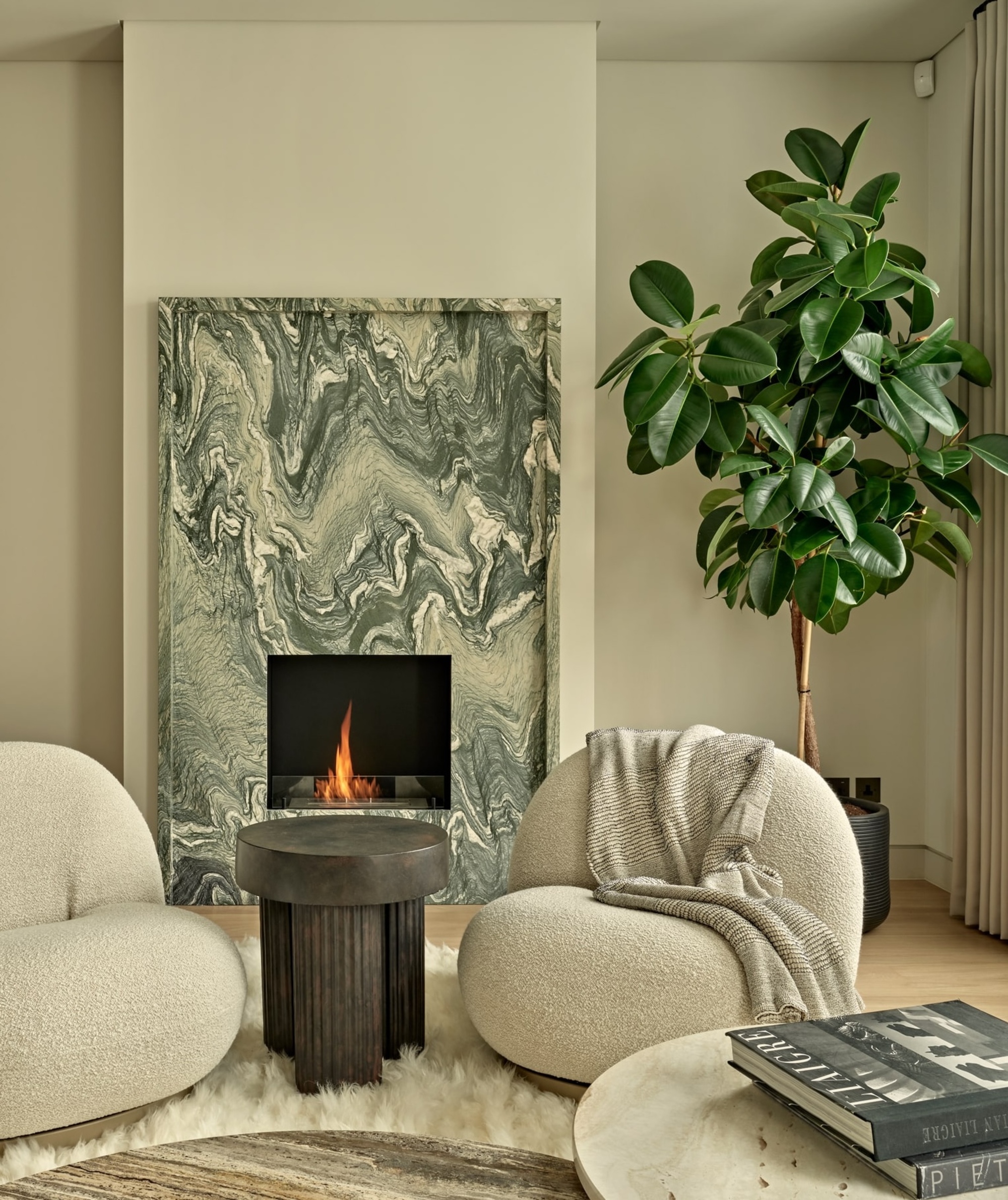 beige living room with grey and green marble fireplace, tall potted fiddle leaf tree, two boucle armchairs (one draped in a gray throw), a dark gray stone side table, and fluffy white rug