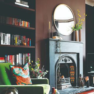 A dark brown-painted living room with a black fireplace and a green accent chair