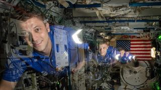 a timelapse image showing an astronaut moving from the back to the front of a module in the international space station. at back is an american flag
