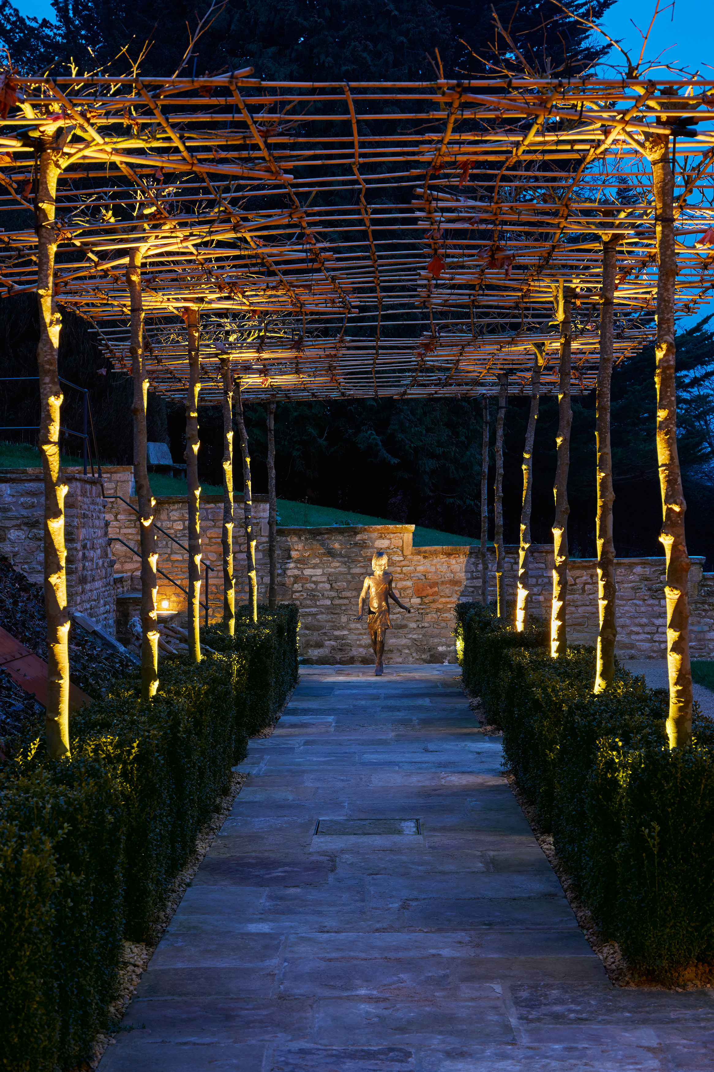 a covered garden path leading to a sculpture of a boy