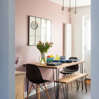 Pink open plan kitchen diner with industrial table and bench with hairpin legs, window mirror, vertical radiator, blue tableware