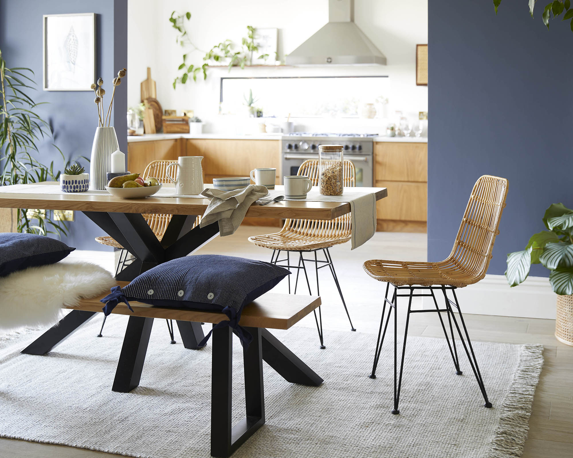 A blue open-plan kitchen-diner with blue wall paint decor, wooden bench and rattan chairs