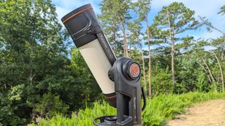 a black and white telescope in a field with trees behind it