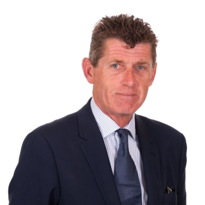 man with short brown hair wearing navy suit, white and blue striped shirt and navy tie