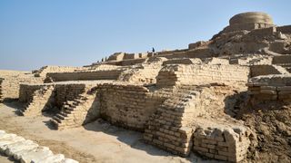 This is a photo of the Indus Valley Civilization's ancient stupa - one of the best preserved parts of Mohenjo Daro in Pakistan. It is a series of large steps made out of sand-colored bricks, interwoven with staircases. Right at the top is a circular dome.
