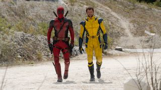Ryan Reynolds in his red Deadpool suit and Hugh Jackman in yellow Wolverine suit walking through desert setting in Deadpool & Wolverine.