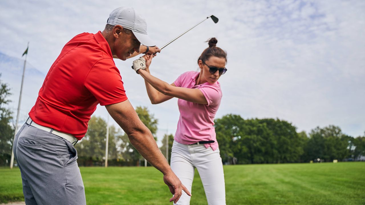 Golf pro teaching a female golfer