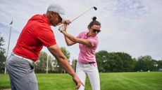 Golf pro teaching a female golfer