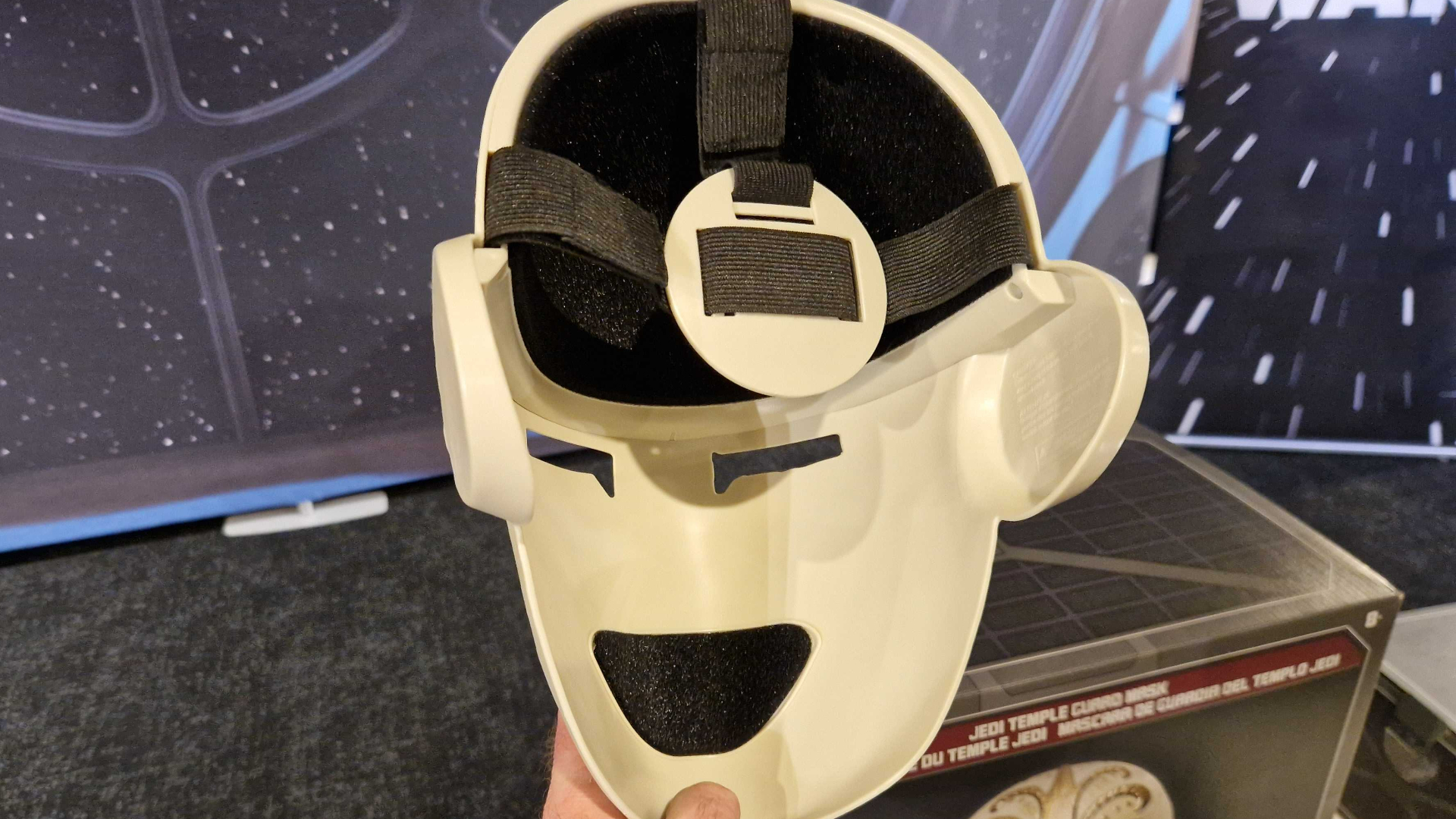 Star Wars Jedi Temple Guard Mask seen from behind, held by a hand against a starry background