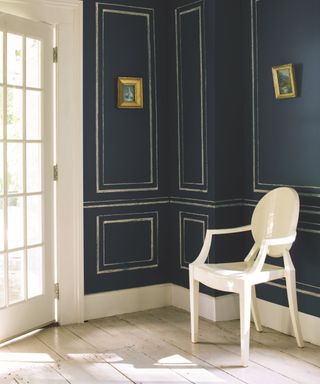 dark blue panelled walls in corner of room with light wood floors, white accent chair and glass door