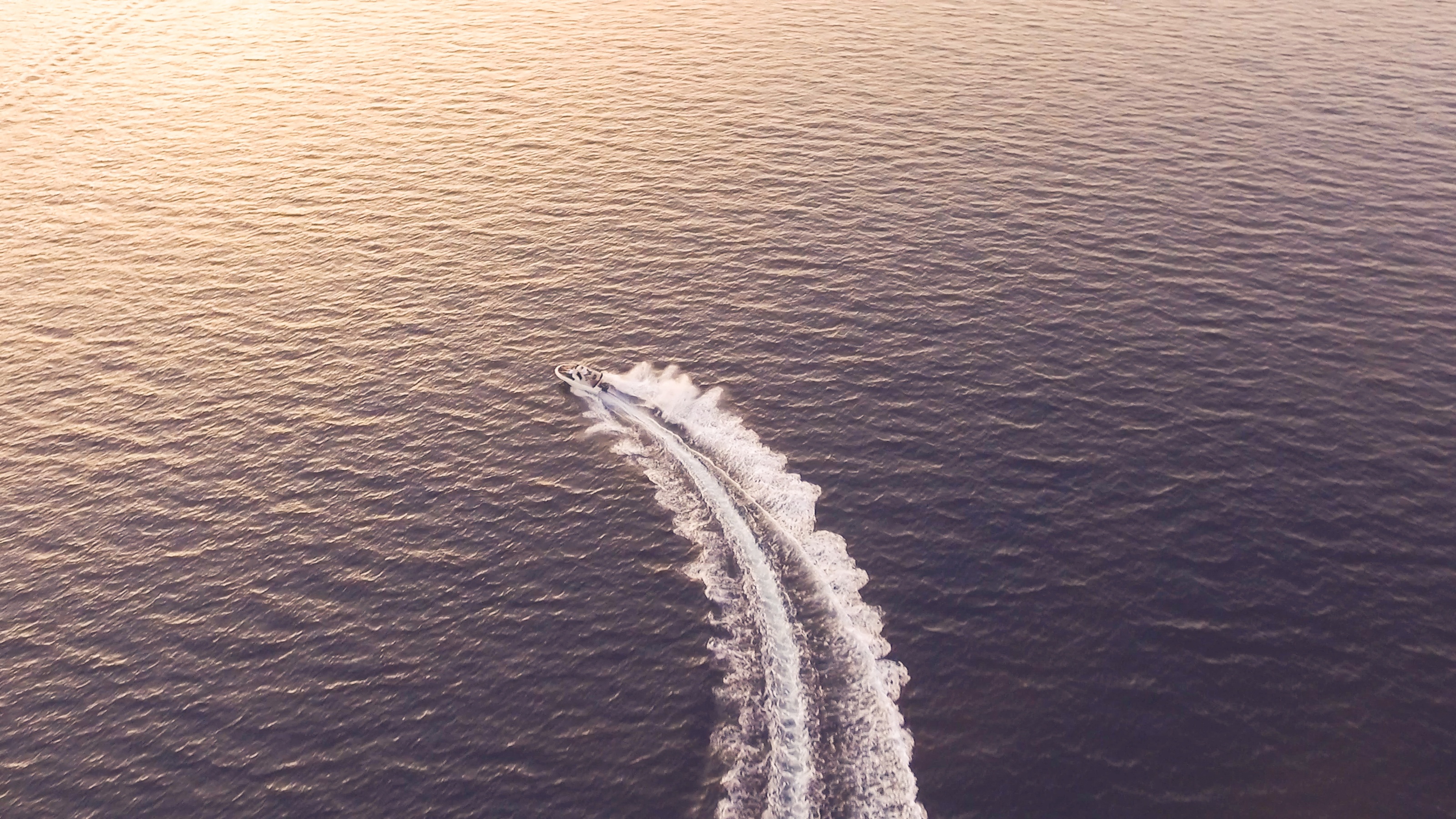 A boat speeds across water toward a sunset.