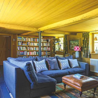 Living room with yellow wooden ceiling, blue painted floorboards and blue L-shaped sofa. Hawthbush Farm, a 17th century five-bedroom former hop farm with 140 acres of land in East Sussex.