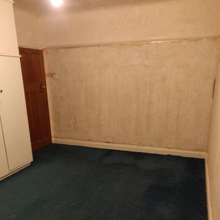 Before photo stripped empty bedroom with bare walls dark carpet and brown door