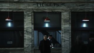 Burt walking away from ticket booth at train station in Severance