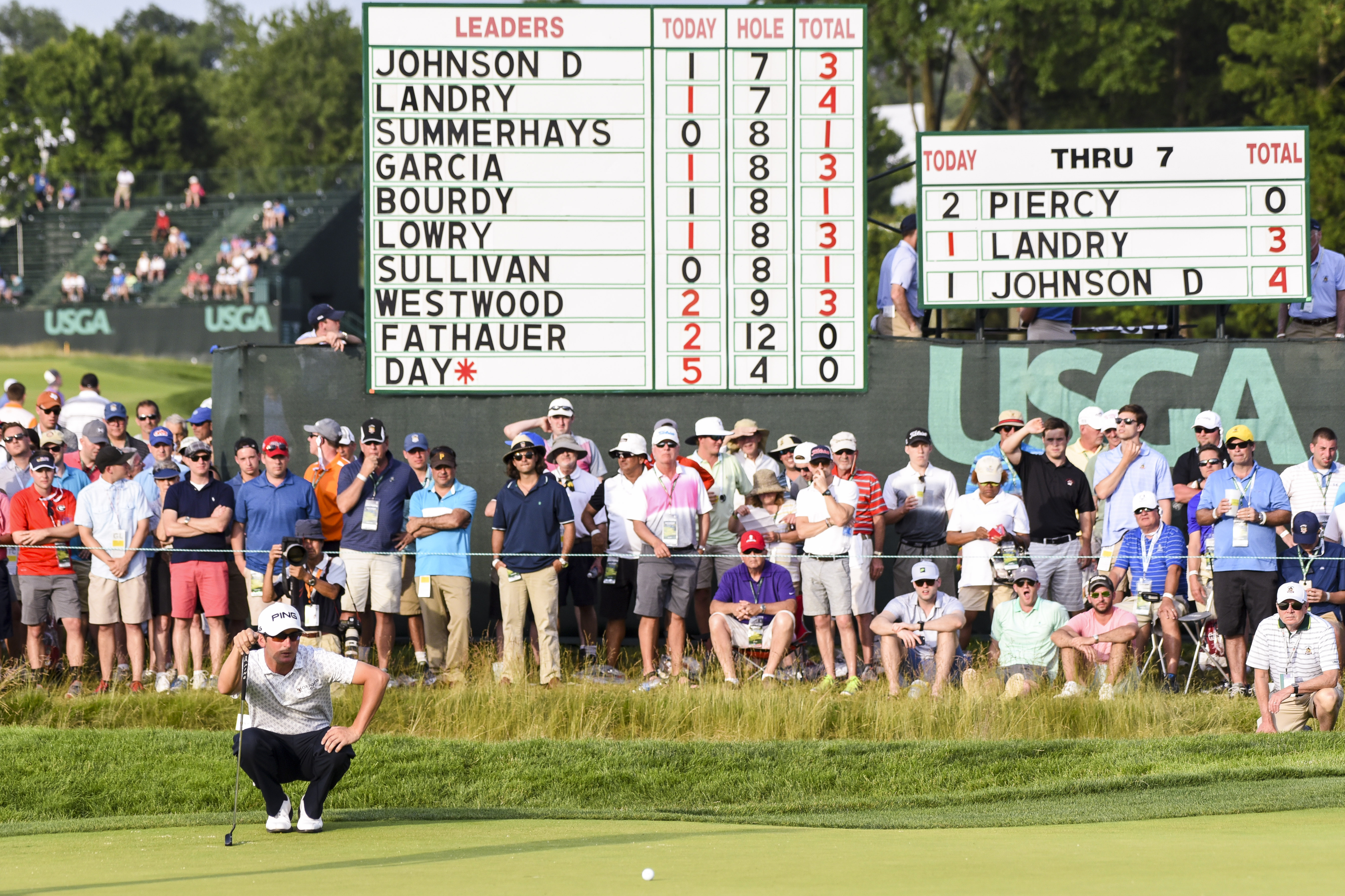 Andrew Landry crouches down behind a putt at the 2016 US Open with a leaderboard showing his name at the top behind
