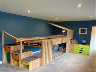 A kids bed designed in wood, with three steps and a play area underneath
