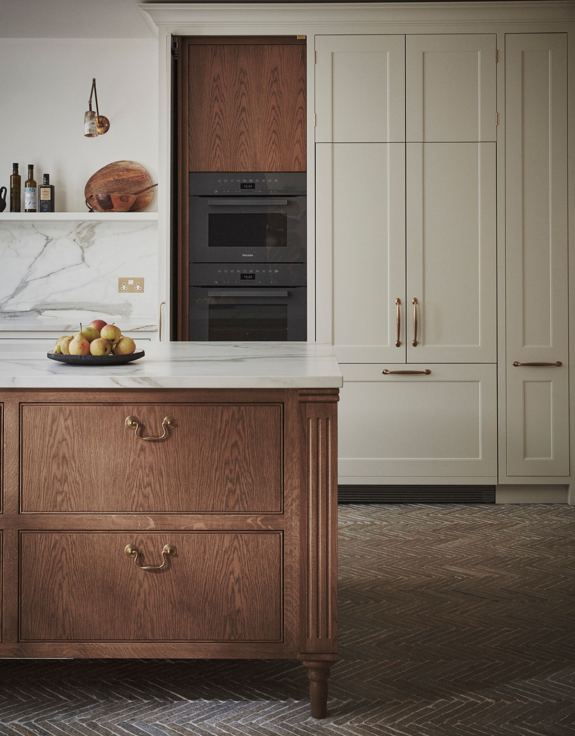 A modern kitchen with off-white built-in cabinetry, marble countertops and a freestanding wooden kitchen island with drawers, gold handles and a marble countertop