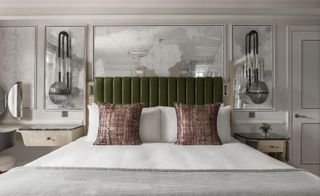 A room in the Mandarin Oriental Hyde Park. Walls with trimming are painted in light gray with an aged mirror decoration and black light fixtures. King size bed is covered with white linen and a gray blanket, while the headboard is in olive green leather.