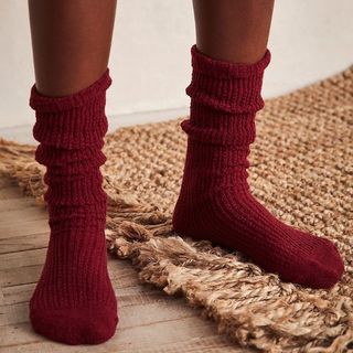 A person standing on a rug wearing a deep red pair of chunky knit socks 