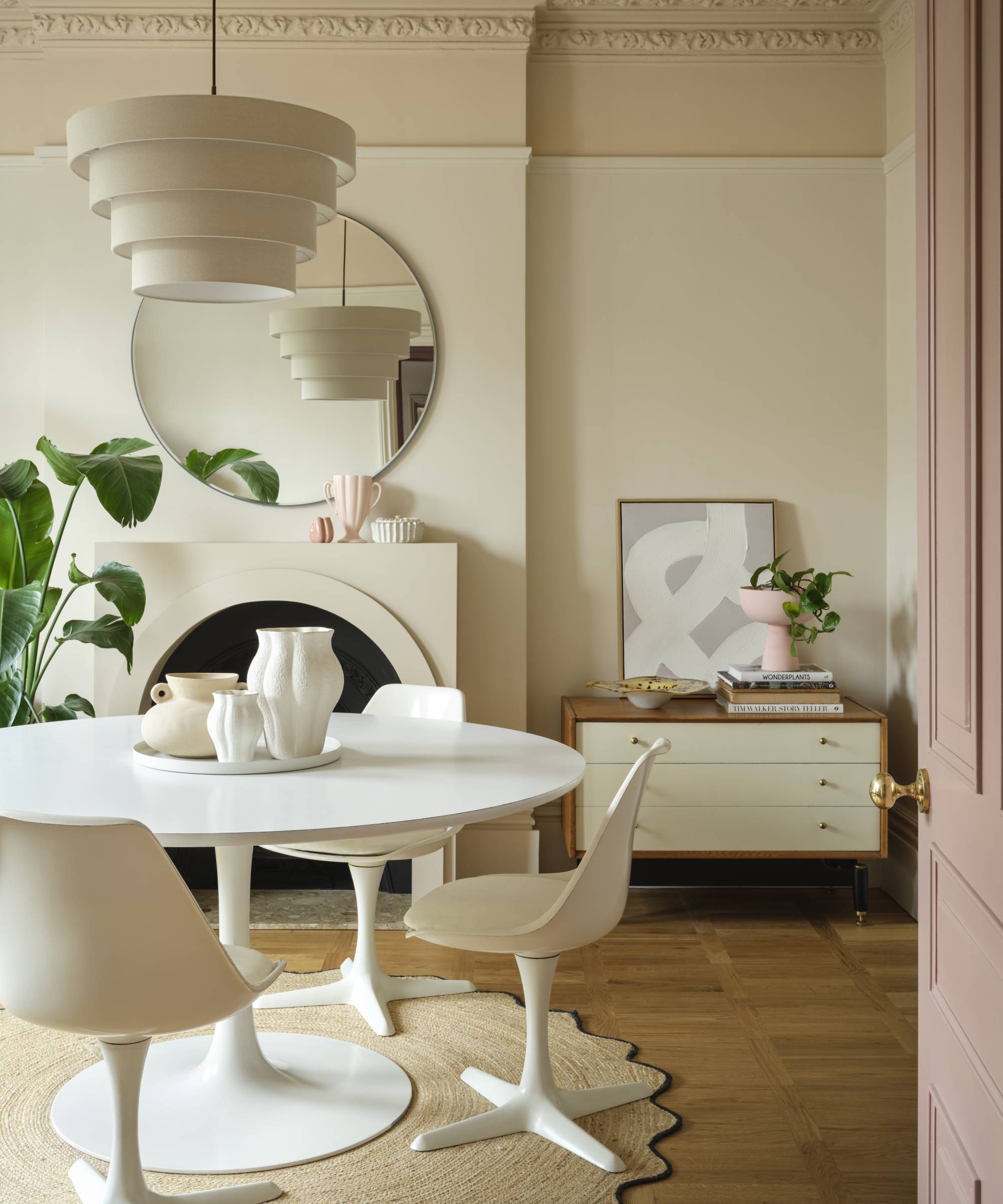 Dining room in shades of cream with white dining table, wooden floor and pink door