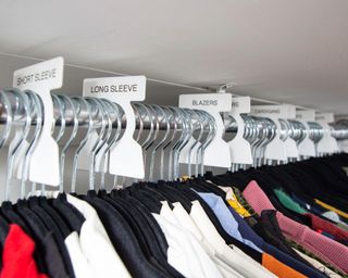 a close up shot of a wardrobe clothing rail with labeled dividers such as blazers