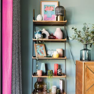 Wooden shelving unit with decorative vases and items displayed on each tier next to pink curtain
