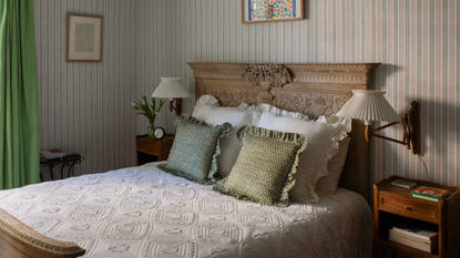 a classic bedroom with striped walls, an ornate bed frame, matching end tables, two sconces, and frilly pillows