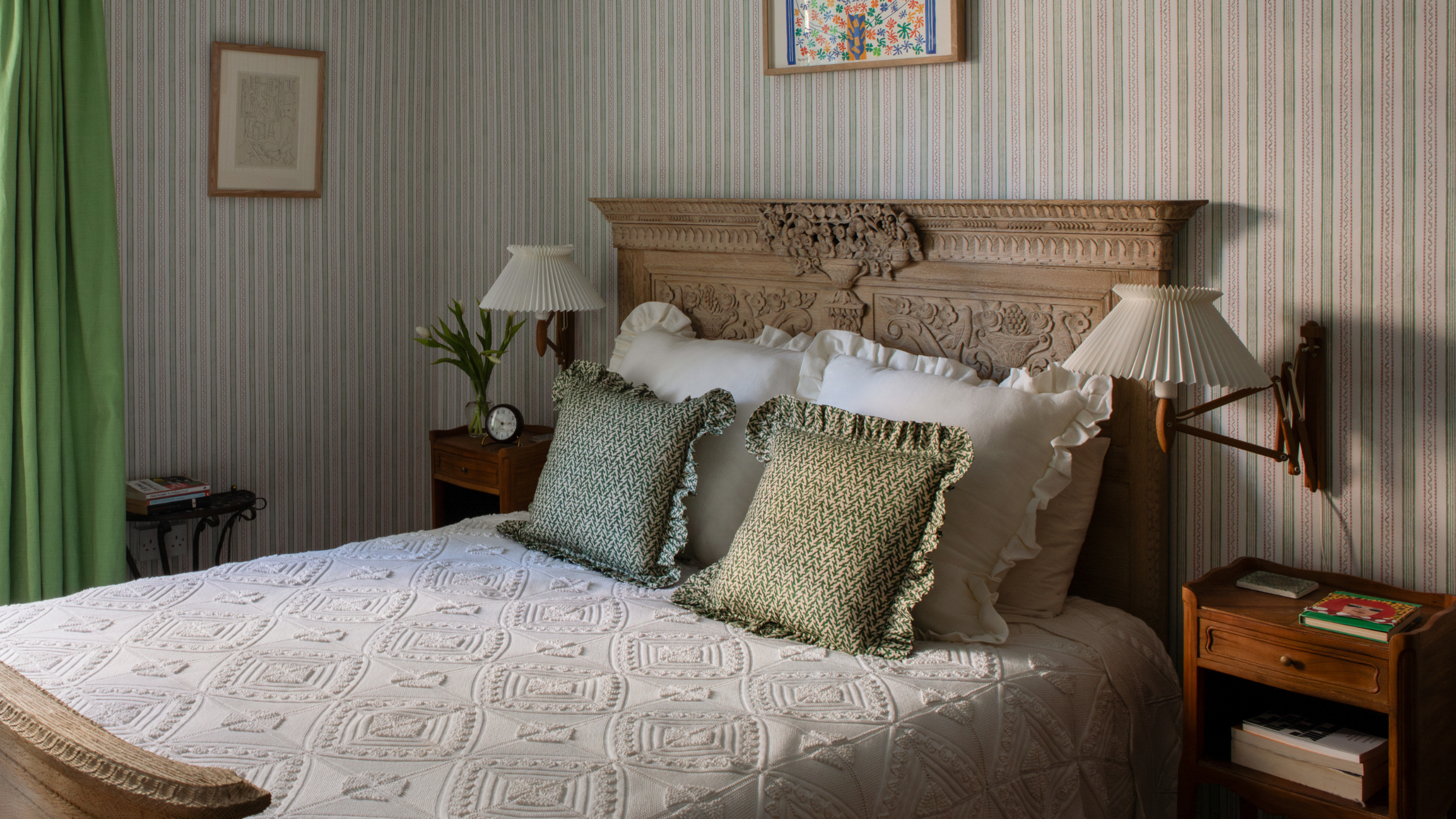 a classic bedroom with striped walls, an ornate bed frame, matching end tables, two sconces, and frilly pillows