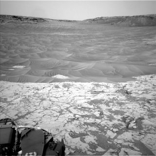Curiosity's Mars rover looked northeast from the lower edge of the pale "Pahrump Hills" outcrop at the base of Mount Sharp on Nov. 13, 2014. Wind-shaped ripples of sand and dust are visible in the middle distance.