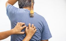 A man gets his back scratched by another person while he also scratches his back with a back-scratcher.