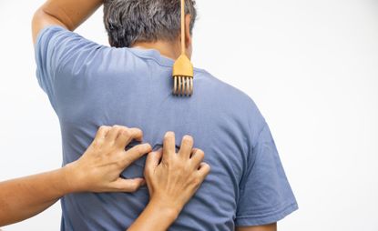 A man gets his back scratched by another person while he also scratches his back with a back-scratcher.