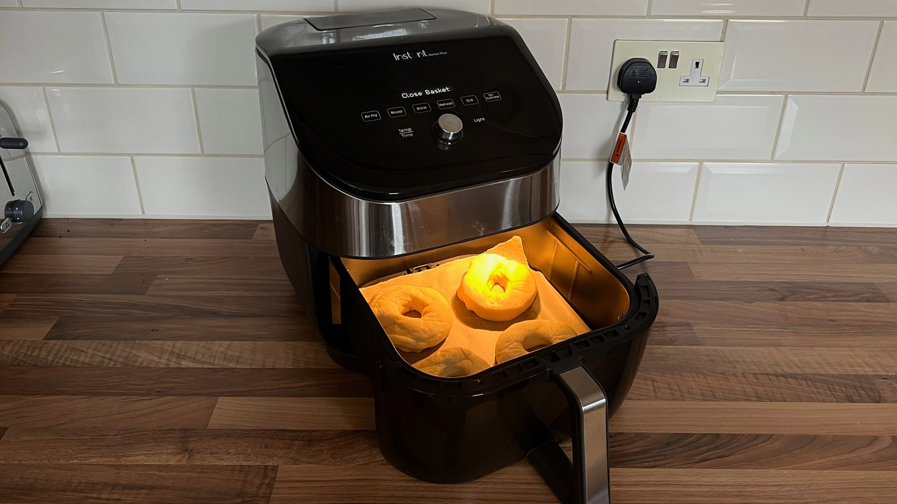 four donuts on greaseproof in the basket of an air fryer waiting to be cooked