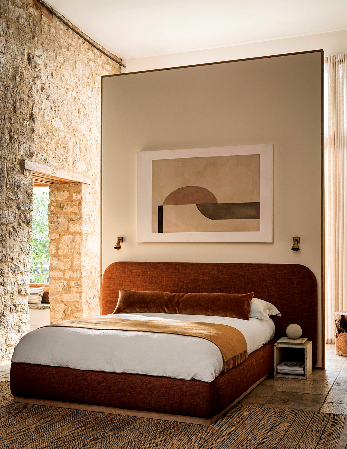 rust colored bed against a partition in a large bedroom with stone walls