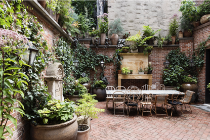 an urban courtyard with various potted plants, brick walls and an antique style table and chairs