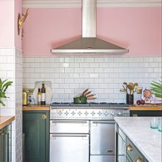 a white a green kitchen with a strip of pastel pink paint behind the extractor fan hood