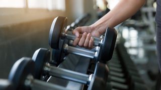 Woman's hands gripping dumbbell and picking it up from the rack