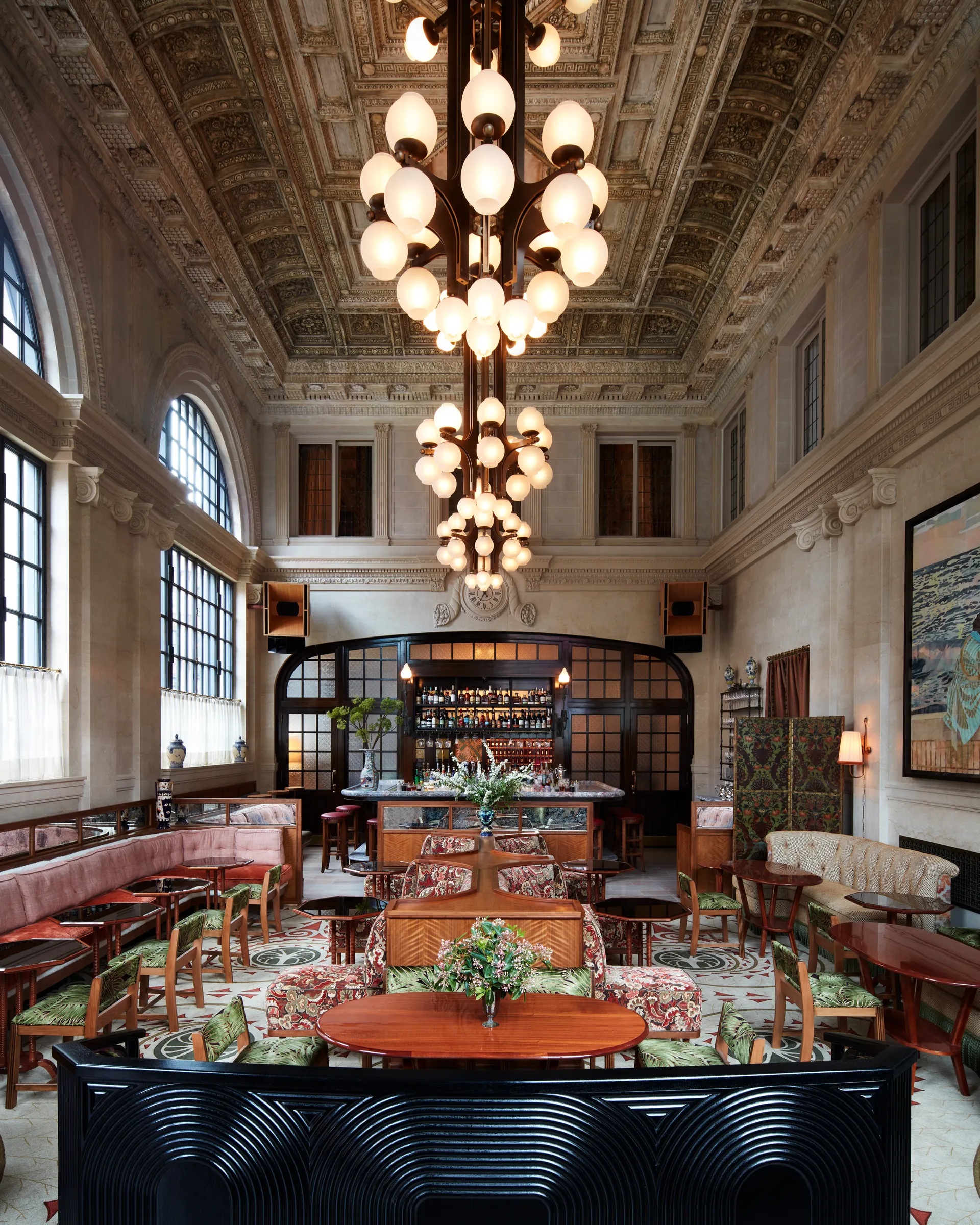 A modern glamour New York hotel boasts spherical Art Deco lighting paired with ornate walls filled with artworks and wooden cabinetry, all infused with soft pastels.