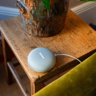 Smart speaker on a wooden side table next to a green velvet sofa