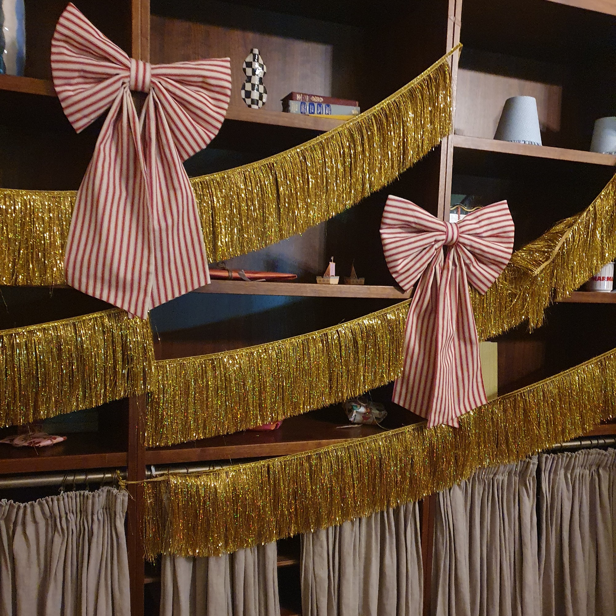 Bookcases decorated with gold fringe tinsel and striped XL bows at the Etsy Christmas 2025 trend event