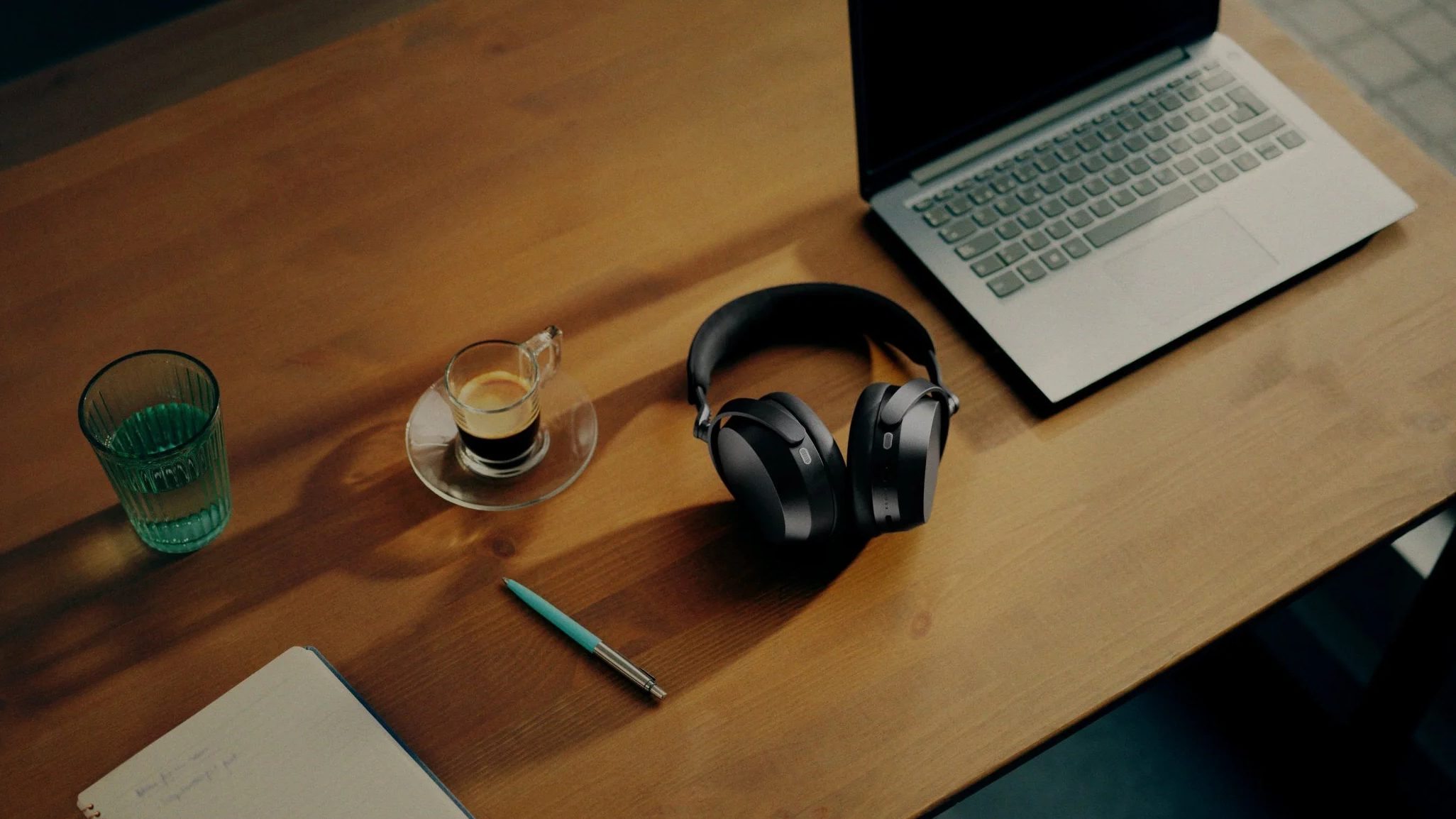 Sennheiser Momentum 5 headphones in situ on table with laptop, coffee, notepad and glass of water