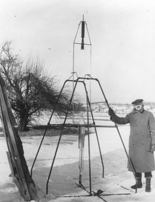 Dr. Robert H. Goddard and a liquid oxygen-gasoline rocket in the frame from which it was fired on March 16, 1926, at Auburn, Mass. The rocket flew to a height of 41 feet and returned to Earth in two and a half seconds.