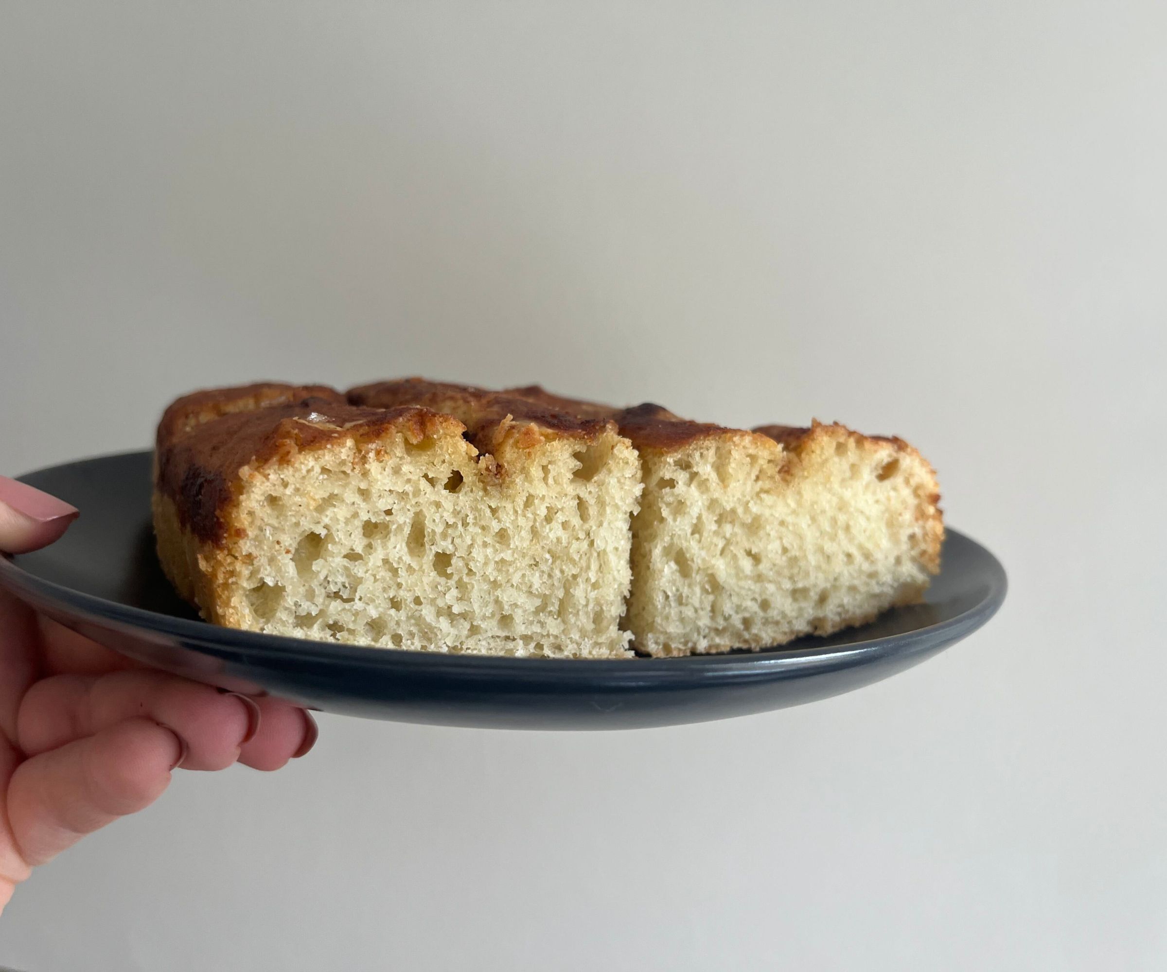 A side view of an airy focaccia dough on a small plate. 