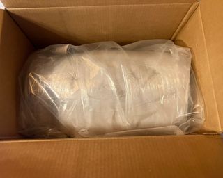 Tempur-Pedic mattress topper rolled up in plastic packaging inside brown cardboard box