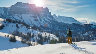 Woman with trekking poles looking out at snowy mountains